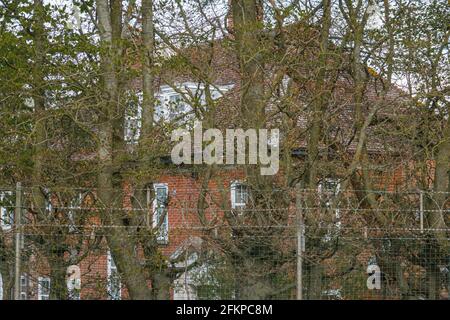 grande casa di campagna inglese appartata dietro gli alberi e protetta da recinzione con filo spinato Foto Stock