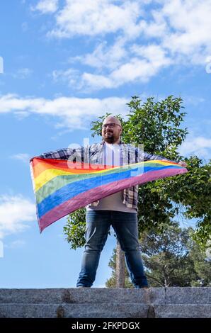Un ragazzo che tiene la bandiera dell'arcobaleno, soffia nel vento. Amore gay. Gay orgoglio giorno Foto Stock