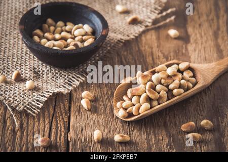 Pinoli su un cucchiaio di legno e in un piccolo ciotola su sfondo di legno Foto Stock