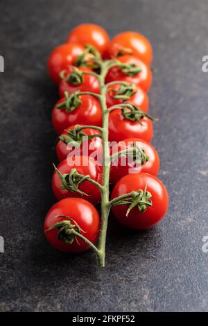 Pomodori ciliegini rossi freschi. Pomodori piccoli sul ramo sul tavolo nero. Foto Stock