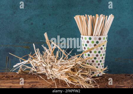 Cannucce da bere di paglia naturale in un becher di bambù e un fascio di paglia su un vecchio fascio di legno, sfondo verde. Concetto di sostenibilità, senza plastica. Foto Stock