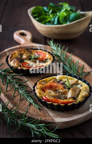 Due tartlet vegetariane su tavola di legno e una ciotola di legno con insalata di campo fresco su un tavolo rustico, foto verticale stock Foto Stock