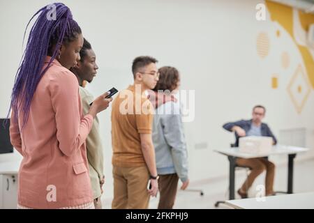 Gruppo vario di allievi che si levano in piedi in linea per consultare il professore maturo dell'università nell'auditorium della scuola, spazio di copia Foto Stock
