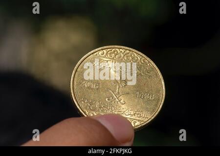 Mano del bambino asiatico che tiene una cinquanta moneta di Riyal di Halalas, soldi dell'Arabia Saudita, fuoco selezionato e sfondo scuro Foto Stock