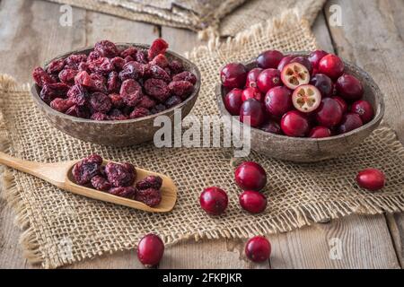 Mirtilli rossi crudi ed essiccati in conchiglie di cocco e su a. cucchiaio di legno su tavolo di legno Foto Stock