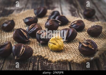 Castagne arrostite, una sbucciata, su sfondo di legno scuro Foto Stock