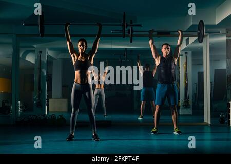 Una coppia di allenamento allenarsi in palestra e fare esercizio di squadra in testa con il peso sul barbell. Foto Stock