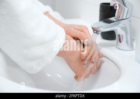 Primo piano di giovane donna con manicure alla moda lavando le mani a casa in bagno. Concetto di cura di processo per mani e corpo con speciali creme e soa Foto Stock