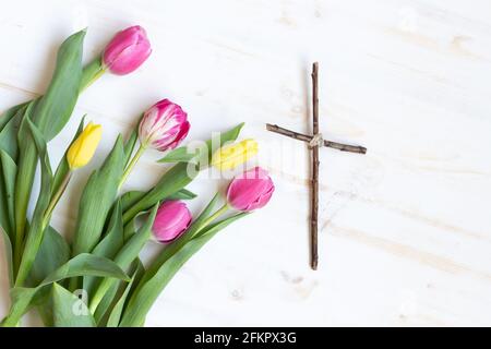 piccola croce cristiana di legno su sfondo bianco di legno con fresco tulipani rosa e giallo Foto Stock