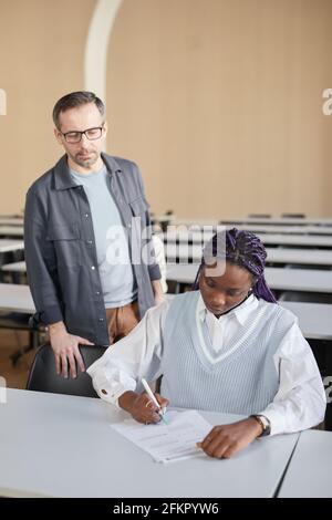 Ritratto verticale di giovane afroamericana che prende esame all'università con il professore che la guarda, spazio di copia Foto Stock