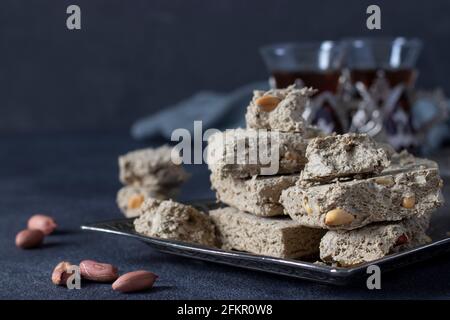 Halva dolce di girasole con arachidi su vassoio di metallo su sfondo grigio scuro. Primo piano Foto Stock