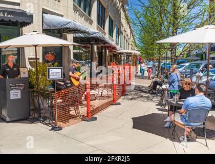 ASHEVILLE, NC, USA-1 MAGGIO 2021: Persone che siedono ai tavoli e alle panchine di Carmel su Page St. In un giorno di sole, primavera. Maschere di protezione visibili. Foto Stock