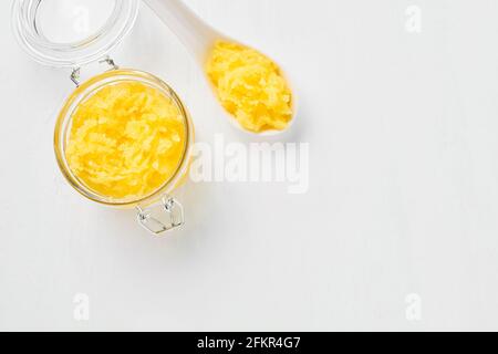 Scrub del corpo giallo fatto in casa in un vaso di vetro su sfondo bianco. Concetto DI SPA. Messa a fuoco selettiva, vista dall'alto, spazio di copia per il testo. Foto Stock