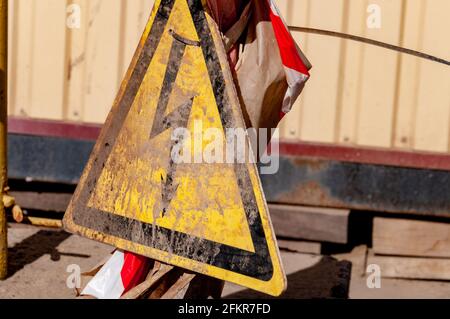 Segnale di attenzione a forma di triangolo relativo al pericolo di alta tensione. Segnale di pericolo schizzato da sporcizia. Simbolo di avvertenza. Cartello stradale industriale vicino. D. Nero e giallo Foto Stock