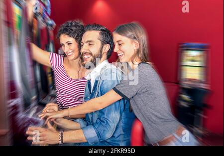 Felici i giovani amici che si divertono insieme con slot machine - Concetto di gioco d'azzardo con le persone che giocano a cash dispositivi automatici in casinò e resort moderni Foto Stock