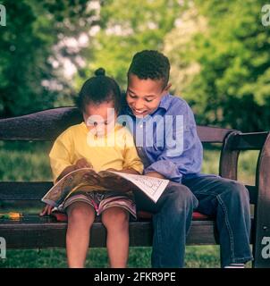Fratelli fratelli e sorelle 7 anni e 4 anni British African Caribbean, al di fuori insieme con fratello aiutare sua sorella con le sue attività di libro da colorare. Foto Stock