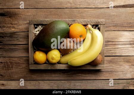 Frutta tropicale fresca in una scatola di consegna di legno su sfondo di legno. Arancione, banana, mango, kiwi e limone vista dall'alto piatto con spazio per la copia per som Foto Stock