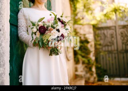Sposa tiene in mano un bel bouquet di fiori appoggiandosi contro la porta verde dell'edificio Foto Stock