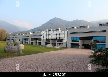 Scuola Media, scuola media a Morbio inferiore, Svizzera. Scuola di architettura moderna con scultura a piedi di fronte e montagne sullo sfondo Foto Stock