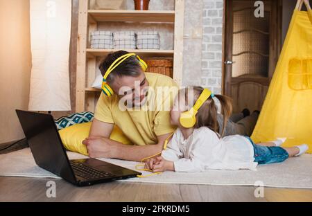 un padre e la sua bambina si trovano sul pavimento con cuffie gialle e si guardano a vicenda. giochi congiunti con i bambini Foto Stock