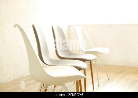 Consulenza di terapia di gruppo per tossicodipendenti e concetto alcolico. Poltroncine vuote in stile loft multiplo, bianche e grigie, in piedi in fila su pavimento in legno testurizzato. Fou Foto Stock