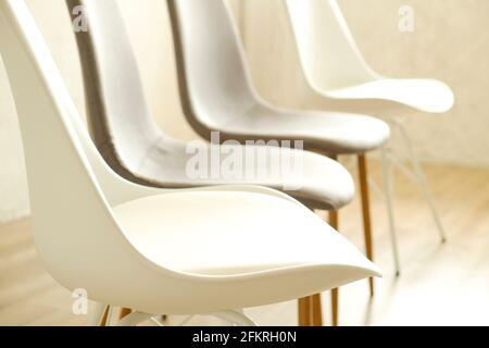 Consulenza di terapia di gruppo per tossicodipendenti e concetto alcolico. Poltroncine vuote in stile loft multiplo, bianche e grigie, in piedi in fila su pavimento in legno testurizzato. Fou Foto Stock