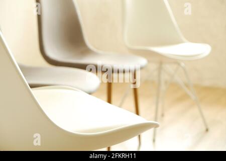 Consulenza di terapia di gruppo per tossicodipendenti e concetto alcolico. Poltroncine vuote in stile loft multiplo, bianche e grigie, in piedi in fila su pavimento in legno testurizzato. Fou Foto Stock