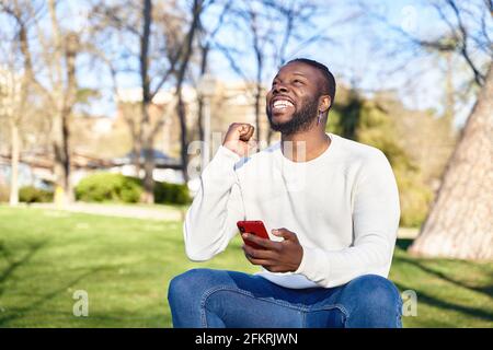 L'uomo afroamericano festeggia le buone notizie guardando il suo telefono cellulare. Concetto di felicità. Foto di alta qualità Foto Stock