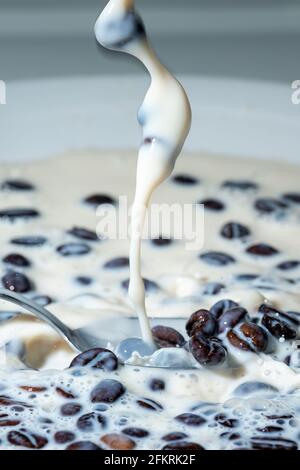 I chicchi di caffè cadono sullo spruzzi di latte. Tazza di latte. Fotografia concettuale. Foto Stock