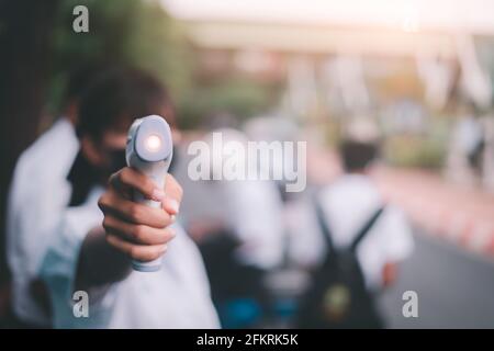 Giovane ragazza usa termometro a infrarossi pistola fronte test di temperatura a. controllare lo studente per proteggere i sintomi del virus covid-19 nella scuola Foto Stock