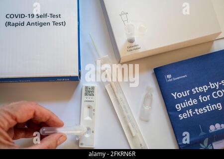 Contenuto del kit di autotest NHS Covid-19 Rapid Antigen; una donna che rilascia il liquido di prova sulla cassetta di test dell'antigene. Foto Stock
