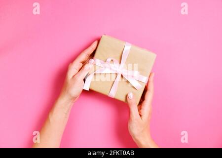 Giovane donna che tiene un singolo presente avvolto a mano in carta artigianale bianco confezione regalo, arco satinato. Mani femminili, giftbox semplice, wrapping, giftwrap, Foto Stock