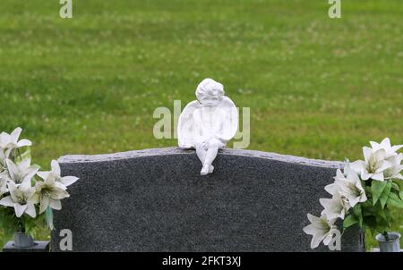 statua di cherubino scultura su cimitero non segnato con il contrassegno di pietra di testa cimitero con con fiori Foto Stock