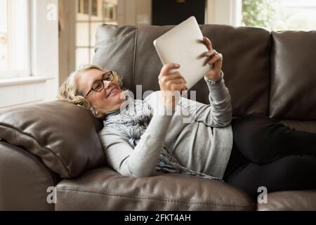 Senior donna sdraiata su un divano guardando a tavoletta digitale Foto Stock
