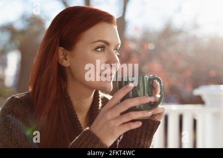 Giovane donna che beve caffè e che guarda fuori dal portico Foto Stock