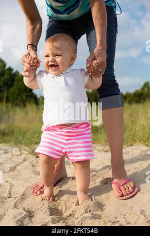 Metà donna adulta holding baby figlie mani mentre toddling in sabbia Foto Stock