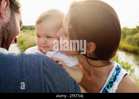 Sulla spalla vista della metà i genitori adulti kissing bimba su Riverside Foto Stock