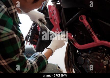 Giovane uomo che fissa una moto nel garage con sfondo. Foto Stock
