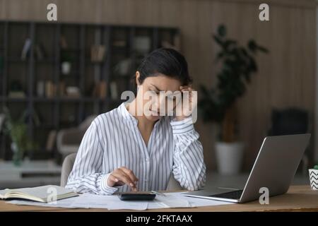 Infelice donna indiana che controlla le fatture domestiche a casa, usando la calcolatrice Foto Stock