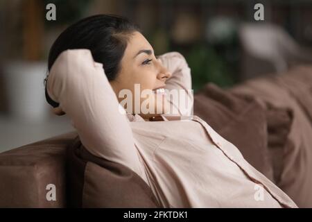 Primo piano sorridente donna indiana che si rilassa, appoggiandosi sul divano Foto Stock