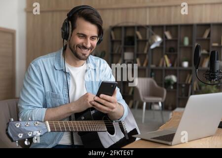Sorridente uomo in cuffia con smartphone, seduto con la chitarra Foto Stock