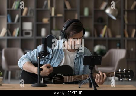 Uomo in cuffia che suona la chitarra acustica, registrando video sullo smartphone Foto Stock