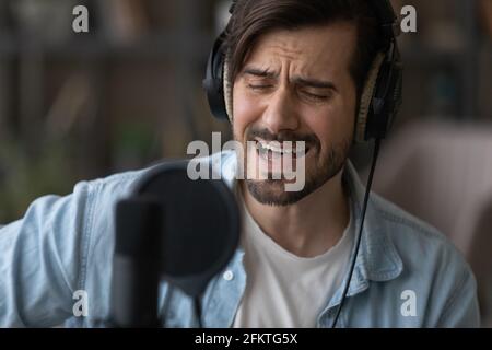 Primo piano cantante uomo in cuffie che cantano, utilizzando microfono professionale Foto Stock