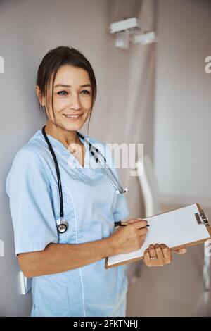 Affascinante dottoressa che scrive sugli appunti in clinica Foto Stock