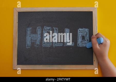Primo piano di una tavola con la parola ciao scritta in gesso in blu con la mano di una ragazza Foto Stock