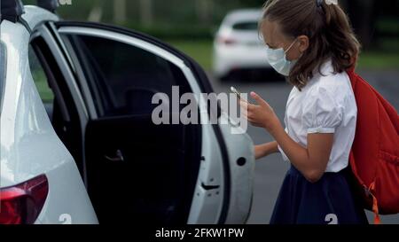 Studenti carini che usano gli smartphone alla scuola elementare. Ragazzo e ragazza in maschere di sicurezza con gadget nelle loro mani. Foto Stock