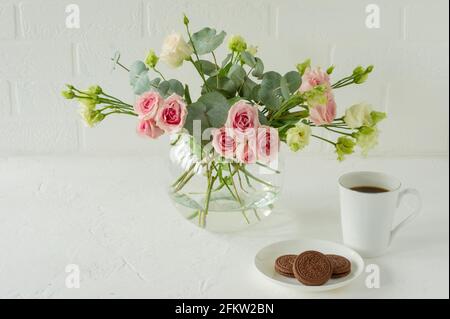 Bouquet di rose, eustoma ed eucalipto in un elegante vaso di vetro su un tavolo. Composizione floreale per decorazioni interne Foto Stock