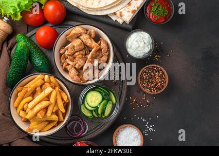 Patatine fritte, carne fritta, cetrioli, pomodori e lattuga su fondo marrone con spazio da copiare. Pranzo, o ingredienti per shawarma, burritos, gyro Foto Stock