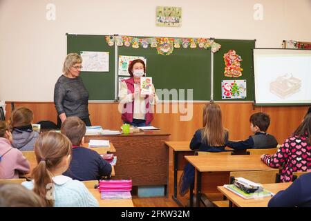 Chapaevsk, regione di Samara, Russia - 23 gennaio 2021: Insegnante di donna in una maschera si trova di fronte alla classe con un libro in mano Foto Stock