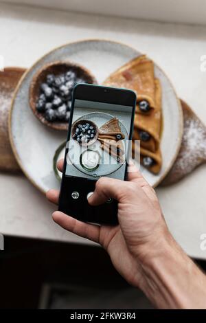 Telefono cellulare fotografia alimentare. Pancake con frutti di bosco. Sfondo bianco Foto Stock